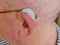 Close up of an elder`s ear with a hearing aid on, a device designed to improve hearing by making or amplifying sound audible to a