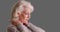 Close-up of elder woman with chronic neck pain looking worried on gray backdrop