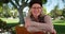 Close up of elder woman with glasses sitting on park bench smiling at camera