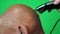 Close-up of an elderly Caucasian man gets his hair cut with a shaving machine, shaving trimer shaves a pensioner`s head, green scr