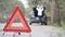 Close-up of emergency stop sign on suburban road with blurred confident Caucasian woman opening car trunk at the