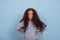 Close up emotional portrait of mulatto frizzy girl wearing blue shirt. She is standing hands in hips and looking angrily at the