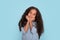 Close up emotional portrait of young mulatta frizzy smiling girl wearing blue shirt on blue background in studio. She holds her