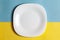 Close-up of an empty ceramic white rounded square plate for mockup. Over yellow blue background