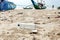 Close up empty used plastic bottle and other waste thrown out at the sea beach on background is fishing boats