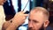 Close up of ending of hairstyling. Cropped barber hands cutting hair with trimmer for bearded man cropped on foreground