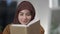 Close-up of engrossed absorbed Middle Eastern young woman reading book smiling and looking at camera. Portrait of