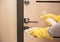 Close up entrance door knob being cleaned with sanitizer spray by female hands in yellow latex gloves, selective focus