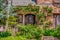 Close-up of entrance to beautiful rock house with arched rustic wooden door surrounded by roses - many old fashioned flowers and a