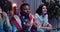 Close up of excited friends holding flags of different countries while sitting on sofa near TV. Multiethnic people