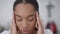 Close-up of exhausted overburdened African American young woman with migraine rubbing temples looking at camera