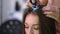 Close-up expert trichologist examining brunette long hair of client with trichoscope. Caucasian professional hairstylist