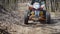 Close up of a extreme rider in green protective equipment and helmet is operating ATV and moving along the road in the