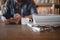 Close up eyeglasses and books stack on wooden desk in university or public library with man using mobile phone reading or text