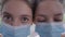Close-up eyes of identical twin sisters in coronavirus face masks looking at camera with serious facial expression