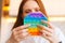 Close-up face of attractive redhead young woman pushing colorful iridescent soft silicone bubbles at home.