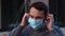 Close-up face of bearded young man wearing medical face mask, looking away on empty city street.