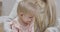 Close-up face of beautiful blond Caucasian baby girl with charming grey eyes. Young mother clapping her daughter`s hands