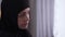 Close-up face of beautiful upset woman in hijab looking out the window at home. Portrait of sad Muslim woman in