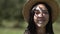 Close-up face of charming Asian young woman with teeth braces in straw hat posing in slow motion outdoors. Headshot