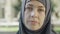 Close-up face of confident attractive Muslim woman in hijab looking at camera outdoors. Portrait of serious beautiful