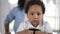 Close-up face of cute African American little boy looking at camera dancing with blurred woman touching curly hair at