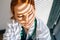 Close-up face of depressed sad young female doctor in white coat sitting on floor hugging legs with hands near window.