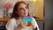 Close-up face of dreaming relaxed redhead young woman pushing colorful iridescent soft silicone bubbles sitting at table