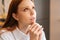 Close-up face of faithful young woman praying holding folded hands in front of face at home, looking up.