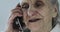 Close-up face of a grandmother with deep wrinkles talking on a mobile phone.