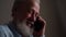 Close-up face of happy gray-haired senior adult male with tears in eyes talking on mobile phone with family at home.