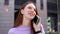 Close up of face of happy red-haired girl talking on phone outdoors in urban background.