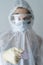 Close-up of the face of a nurse dressed in protective coveralls, mask and glasses offers medication, syringe and pills