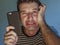 Close up face portrait of young scared and stressed man using mobile phone looking confused feeling worried and frustrated in