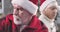 Close-up face of sad old Caucasian man with white beard wearing red Christmas hat looking away. His upset senior wife