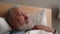 Close-up face of sick gray-haired mature adult male patient lying on bed and telling something to doctor in nursing home