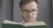 Close-up face of smart young man in eyeglasses reading book. Portrait of bearded brunette Caucasian reader enjoying