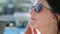 Close-up face of smiling relaxed woman in sunglasses applying sunscreen skin cream during sunbathing