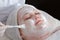 Close-up of the face of a smiling woman in a cosmetology center. Beautician in white medical gloves with a brush applying white