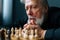 Close-up face of thoughtful gray-haired senior older man thinking game strategy sitting on wooden table with chess board