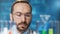 Close-up face of thoughtful male chemical worker looking on beaker with colorful liquid sample