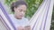 Close-up face of young African American woman sitting in the hammock, relaxing in the garden, texting on cell phone