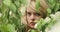Close-up of the face of a young attractive blonde girl between the branches of a flowering tree.