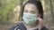 Close-up face of young brunette girl with grey eyes taking off face mask and smiling at camera. Portrait of charming