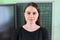 Close-up face of young female teacher near chalkboard and digital screen in classroom