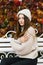 Close-up of the face of a young happy woman enjoying autumn in a hat. She sits on a bench and hugs herself, warming from the cold