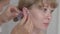 Close-up face of young woman with blurred doctor inserting needles into her ear. Side view portrait of blond beautiful