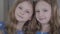Close-up faces of calm Caucasian twin girls looking at camera and smiling. Portrait of nice brunette sisters indoors