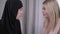 Close-up faces of two women looking at each other. Portrait of modern Caucasian gorgeous lady and conservative Muslim