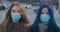 Close-up faces of two young women in protective masks looking at camera at the background of busy city street. Portrait